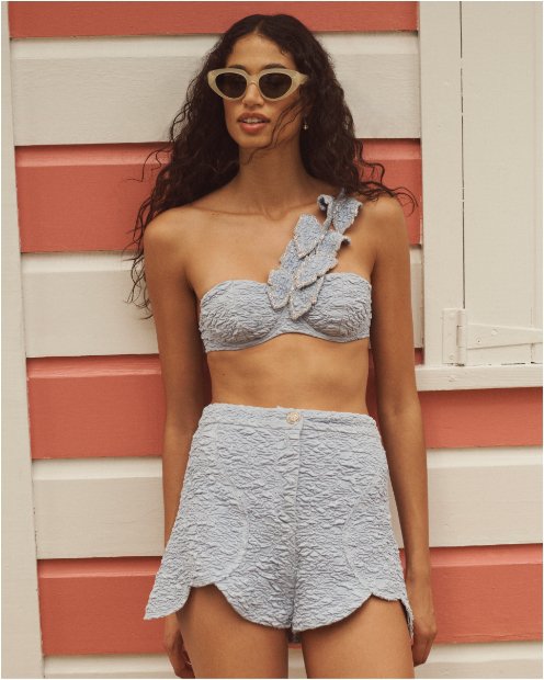A woman in a blue gray one shoulder bikini top and matching swim shorts.